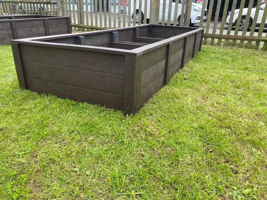 Dark brown recycled plastic 4-bay raised bed planter installed on garden lawn