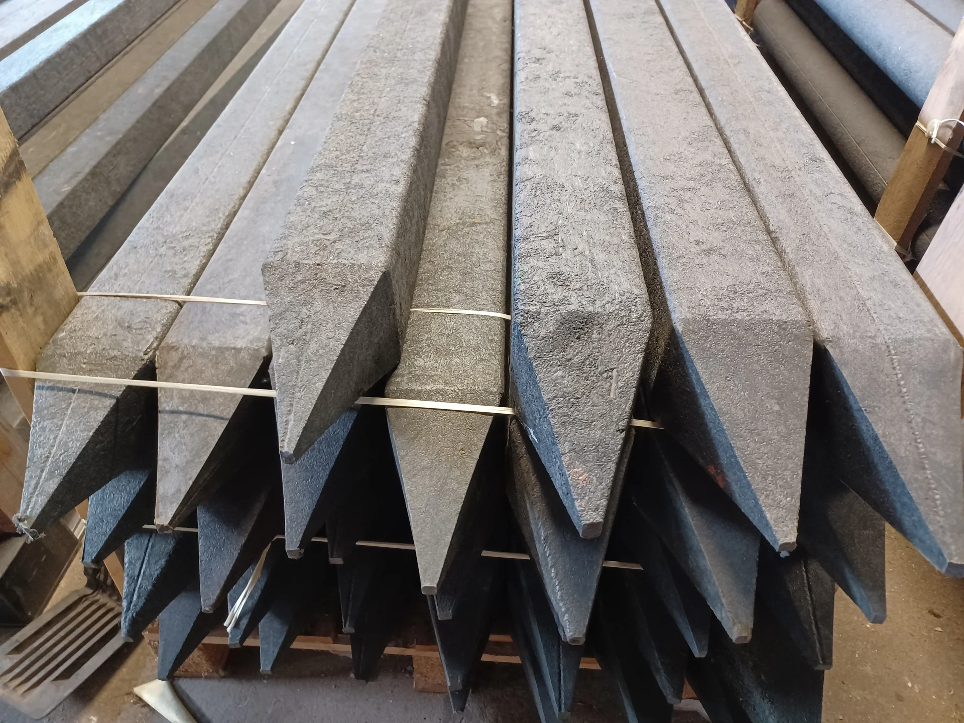 Recycled plastic fence posts with pointed ends stacked at warehouse